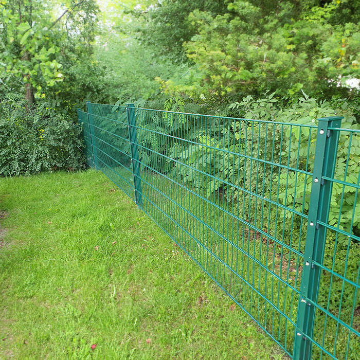 Doppelstabmattenzaun auf Rasen mit Büschen im Hintergrund